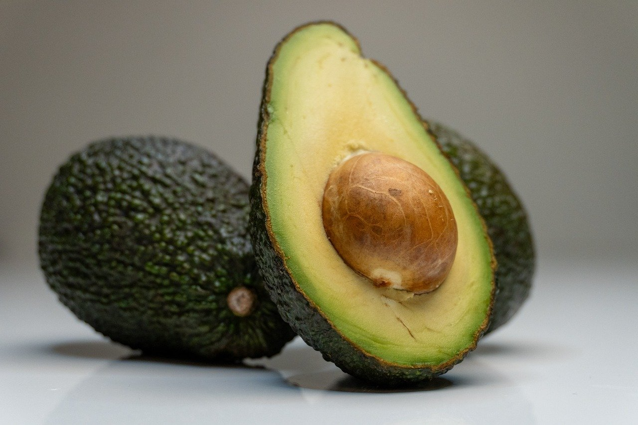 A cut avocado sits in front of two whole avocados