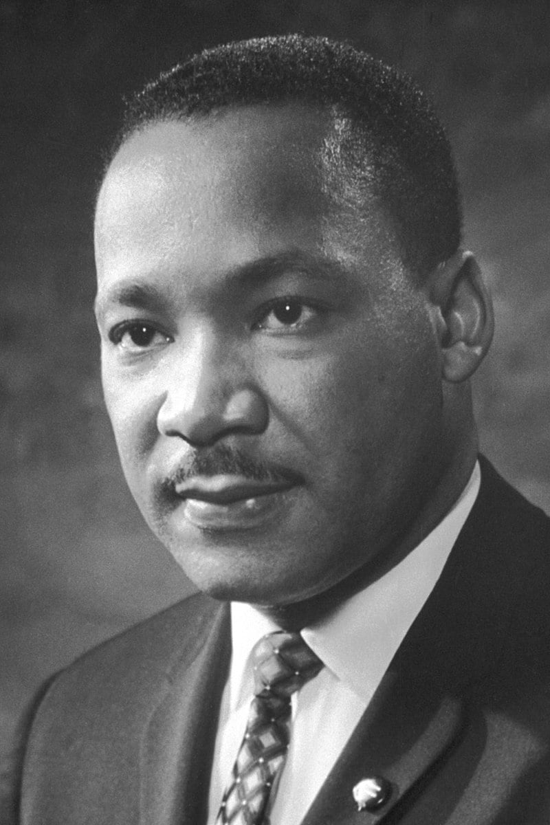 Portrait of a man in a suit and tie, with a calm expression, gazing slightly away from the camera. The background is softly blurred.