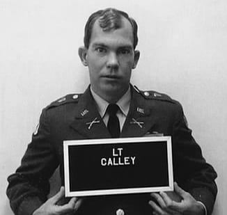 A man in a military uniform holds a sign with "LT CALLEY" printed on it, facing the camera against a plain background.