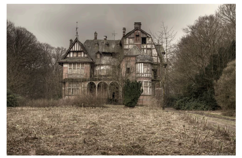 An abandoned Victorian-style manor with cracked windows and overgrown vegetation, surrounded by leafless trees under a cloudy, grey sky.