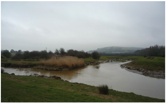 A winding river, with one river joining another, surrounded by green fields and trees.