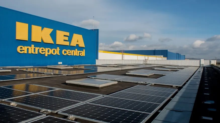 IKEA warehouse with solar panels on the roof, featuring a blue facade and a cloudy sky backdrop, emphasising sustainability initiatives.