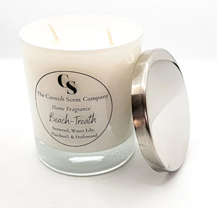 White candle in a glass jar with a silver lid, labelled "The Cornish Scent Company: Beach-Treath", scented with seaweed, water lily, patchouli, and driftwood.
