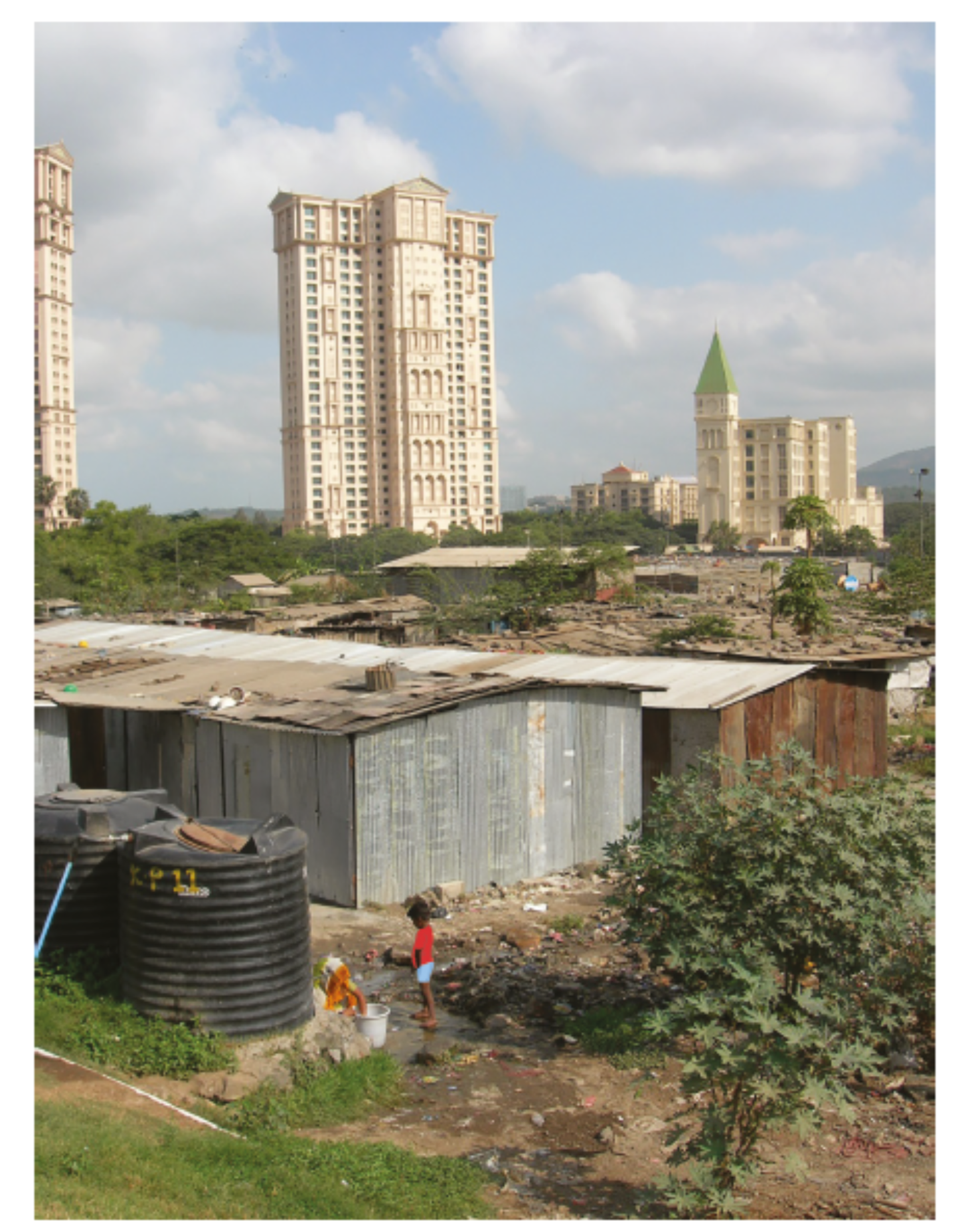 Slum area with corrugated metal shacks in the foreground, juxtaposed against tall, modern buildings and a church spire in the background under cloudy skies.