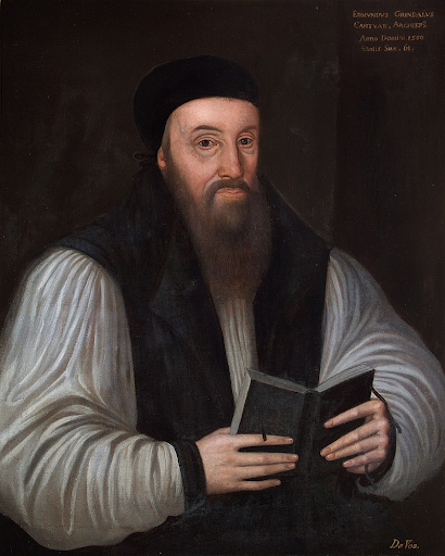 A man in dark robes and a black cap holds an open book, with text in the upper right corner. He has a long beard and a serious expression.