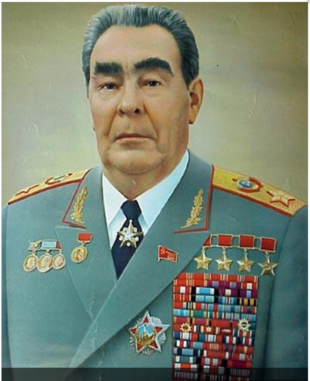 Portrait of a man in a grey military uniform adorned with numerous medals and decorations, against a neutral background.