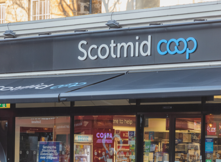 Exterior of a Scotmid Co-op store with grey signage and window display visible. A Costa Express machine is inside near the entrance.