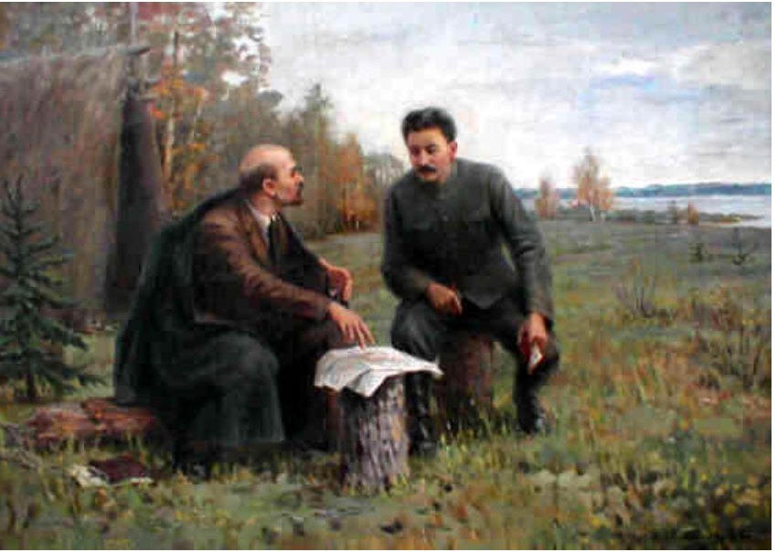 Two men sit outdoors on tree stumps discussing a document, surrounded by grassy landscape near a body of water, with autumn trees in the background.