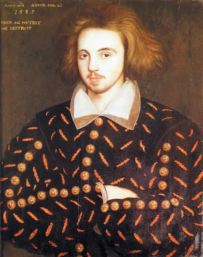 Portrait of a young man with shoulder-length hair, wearing a patterned black coat with gold accents, a white collared shirt, and an unreadable text above.