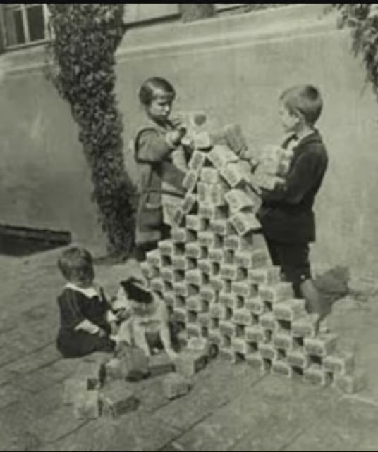 Children building a pyramid with stacked banknotes outside; one child sits with a dog beside a small pile of notes.