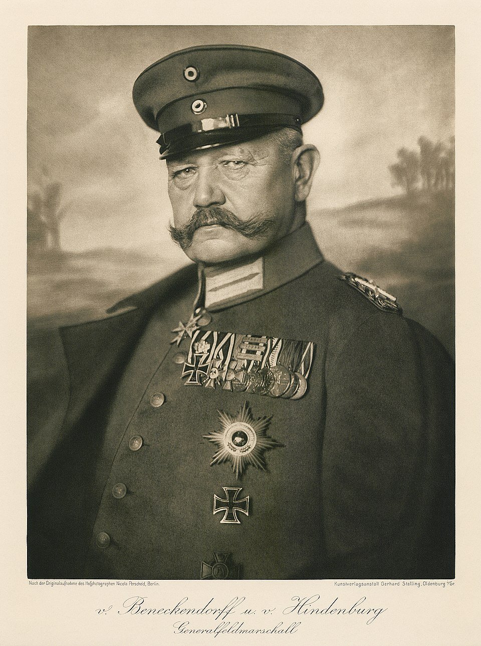 Military officer in formal uniform with prominent moustache, wearing a cap and an array of medals. Background shows a blurred outdoor scene.
