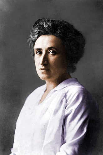 Woman with short dark hair wearing a light-coloured blouse, looking serious against a neutral background.