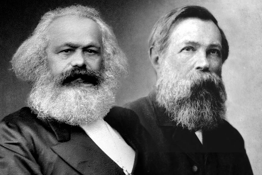 Two historical men, each with a full beard, pose for a black and white photograph against a plain backdrop, dressed in formal 19th-century attire.