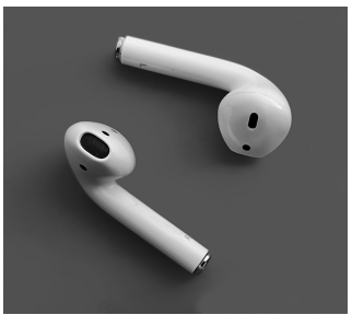 Two white wireless earbuds on a grey background, positioned at angles with visible speakers and charging connectors, showcasing modern design.
