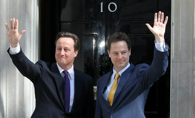 Two men in suits wave outside the iconic black door of 10 Downing Street in daylight, suggesting an official event or meeting.