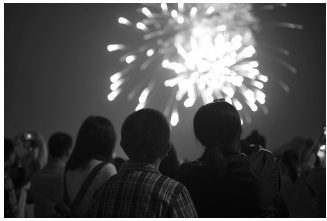 Crowd watching a bright fireworks display in the night sky, with people silhouetted in the foreground capturing the moment with cameras.