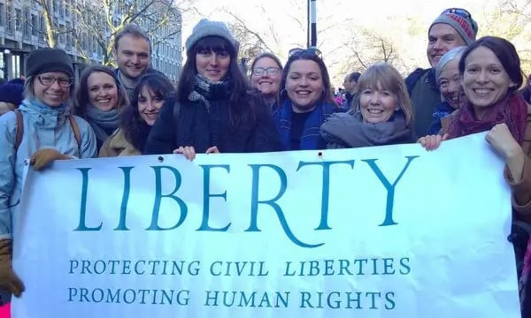 Group of people smiling, holding a “Liberty” banner with text “Protecting civil liberties, promoting human rights” at an outdoor protest or gathering.