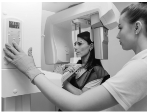 A dental technician assists a patient during an X-ray procedure using a panoramic dental X-ray machine in a clinical setting.