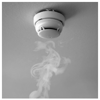 Smoke detector on a ceiling with visible smoke rising, highlighting its function in sensing and alerting to smoke presence for fire safety.