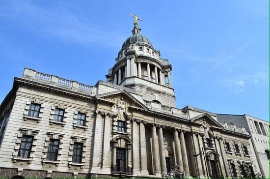 Historic stone courthouse with a large dome, four columns at the entrance, ornate carvings, and a statue on top, set against a clear blue sky.