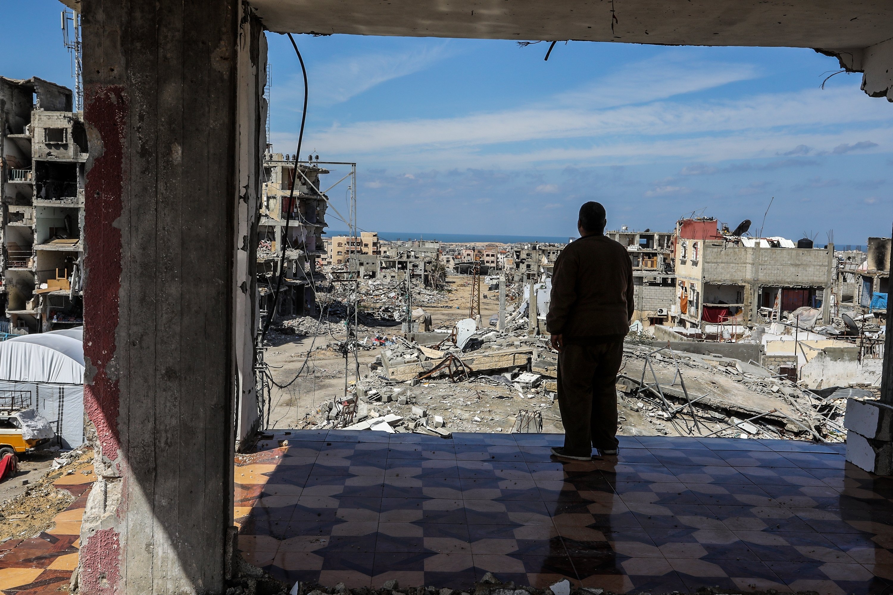The silhouette of a man against a war-torn landscape, with collapsed buildings and rubble