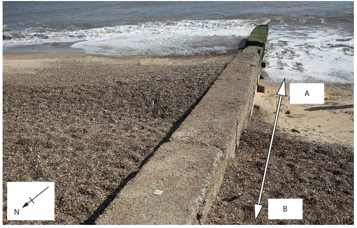 Concrete sea wall leading to the ocean with pebbled beach. Arrows marked A and B indicate direction. Compass in the corner points north.