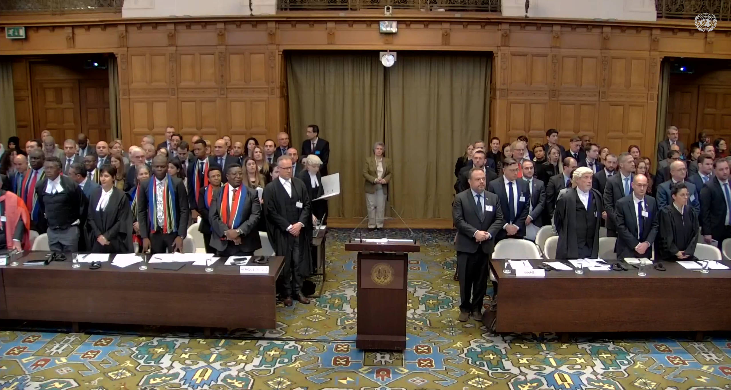 A courtroom scene, with representatives from South Africa on the left and from Israel on the right. An empty lecturn stands central