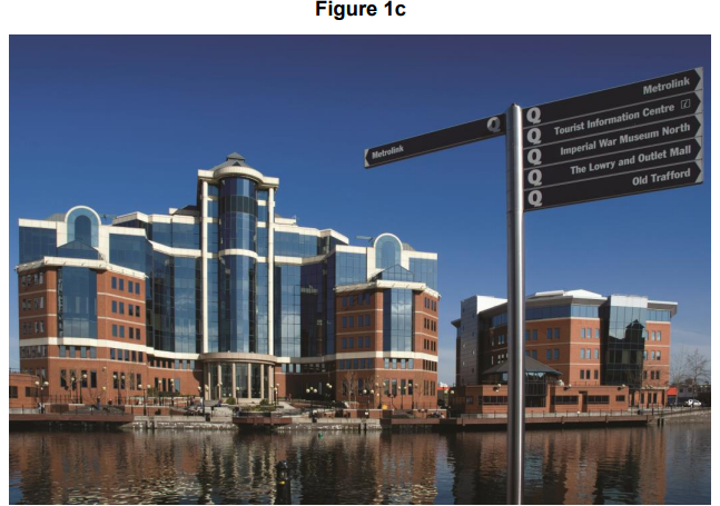 Modern glass and brick building by a canal under a clear blue sky with a black signpost pointing towards tourist attractions like Old Trafford.