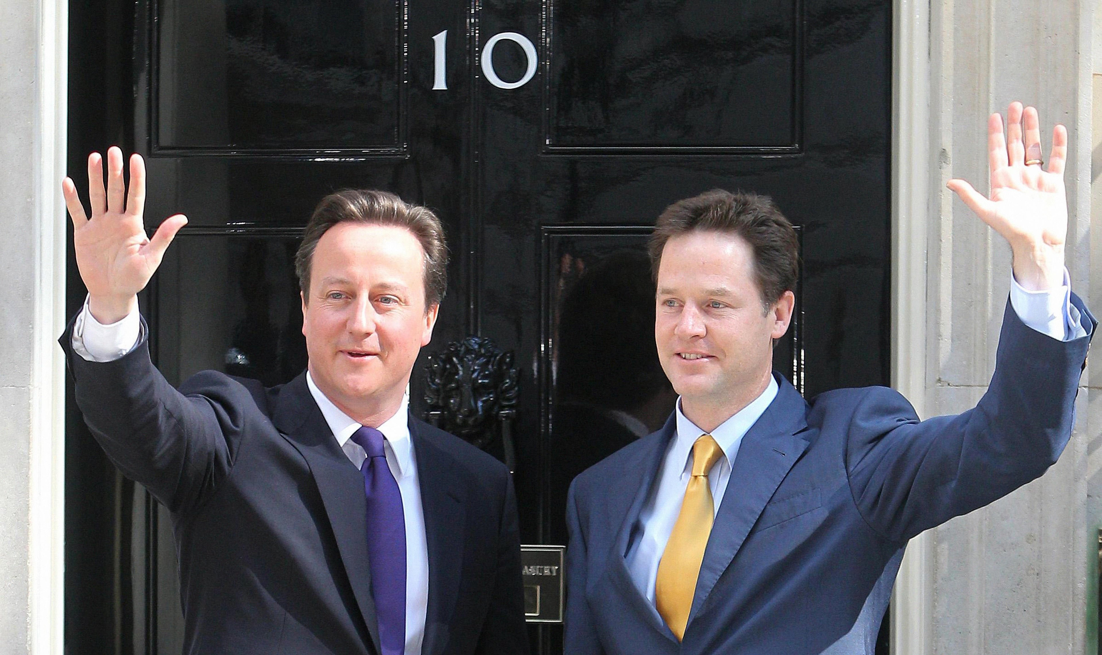 Two men in suits wave outside the black door of 10 Downing Street, under sunlight, with the number "10" visibly prominent above them.
