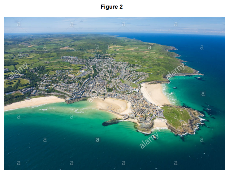 Aerial view of a coastal town with sandy beaches, rocky cliffs, and turquoise sea. Green fields and rural landscape stretch into the distance.
