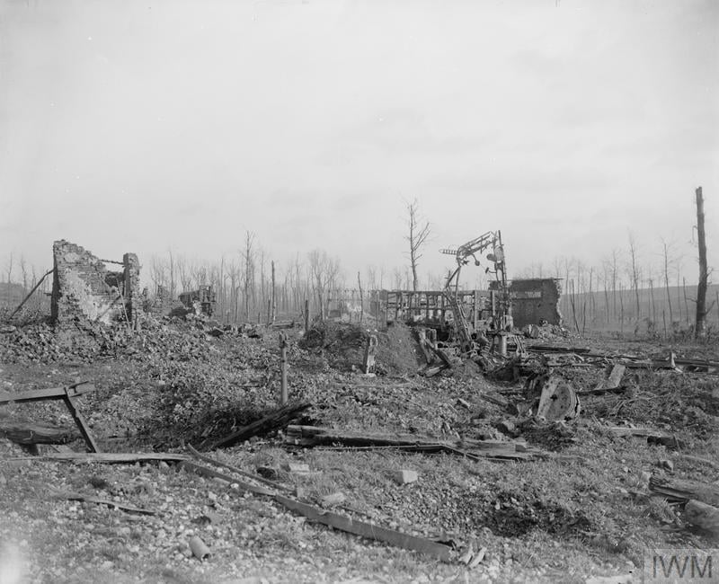 Desolate battlefield with ruined buildings, bare trees, and debris scattered across the ground, depicting the aftermath of warfare under a cloudy sky.
