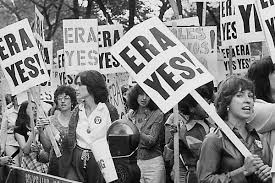 A black-and-white photo of a large group of protestors holding "ERA YES!" signs, advocating for the Equal Rights Amendment, in an outdoor setting.