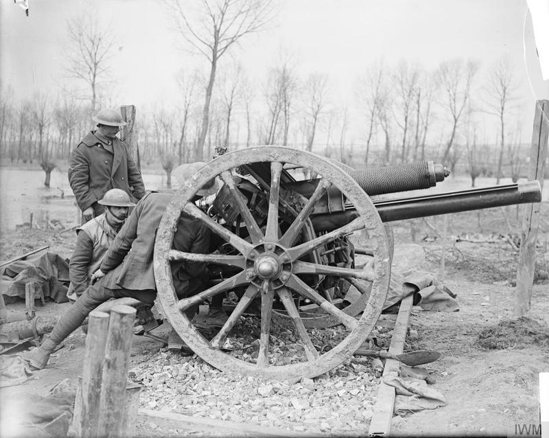 Soldiers operate a field artillery gun in a bare winter landscape, surrounded by leafless trees and muddy terrain, during WWI.