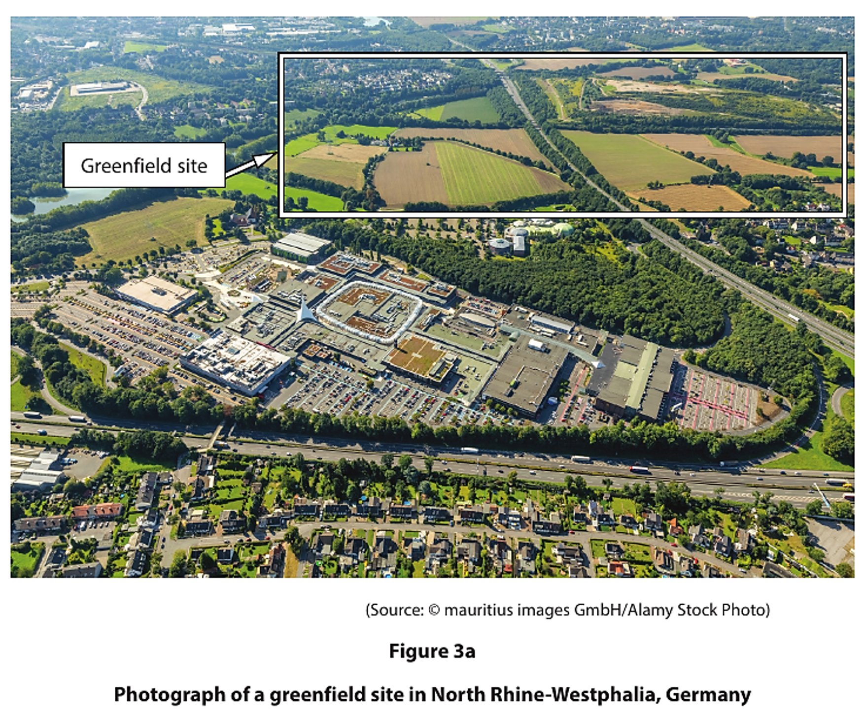 Aerial view of a greenfield site in North Rhine-Westphalia, Germany, with surrounding fields, roads, and a developed area with buildings and car parks.