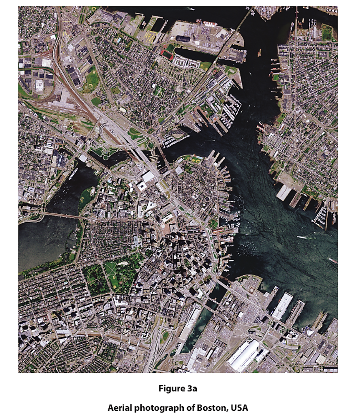 Aerial view of Boston, USA, showing densely packed buildings, roads, bridges, and surrounding waterways, with greenery and urban planning visible.