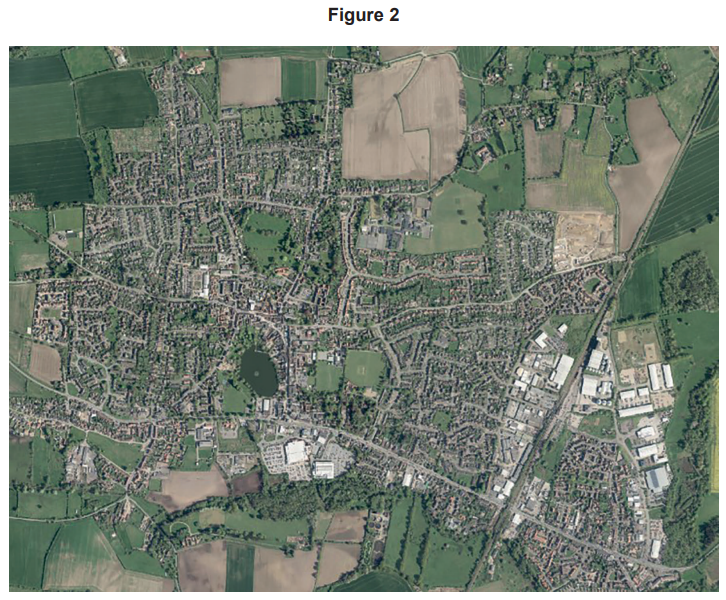 Aerial view of a town featuring residential areas, a central lake, fields, industrial buildings, and roads surrounded by green countryside.