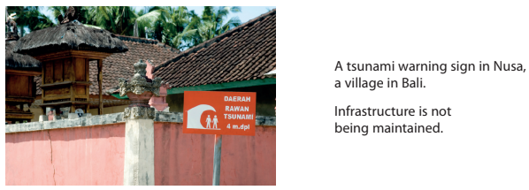 Tsunami warning sign in Nusa, Bali, by a pink wall and traditional thatched roofs; text highlights maintenance issues.
