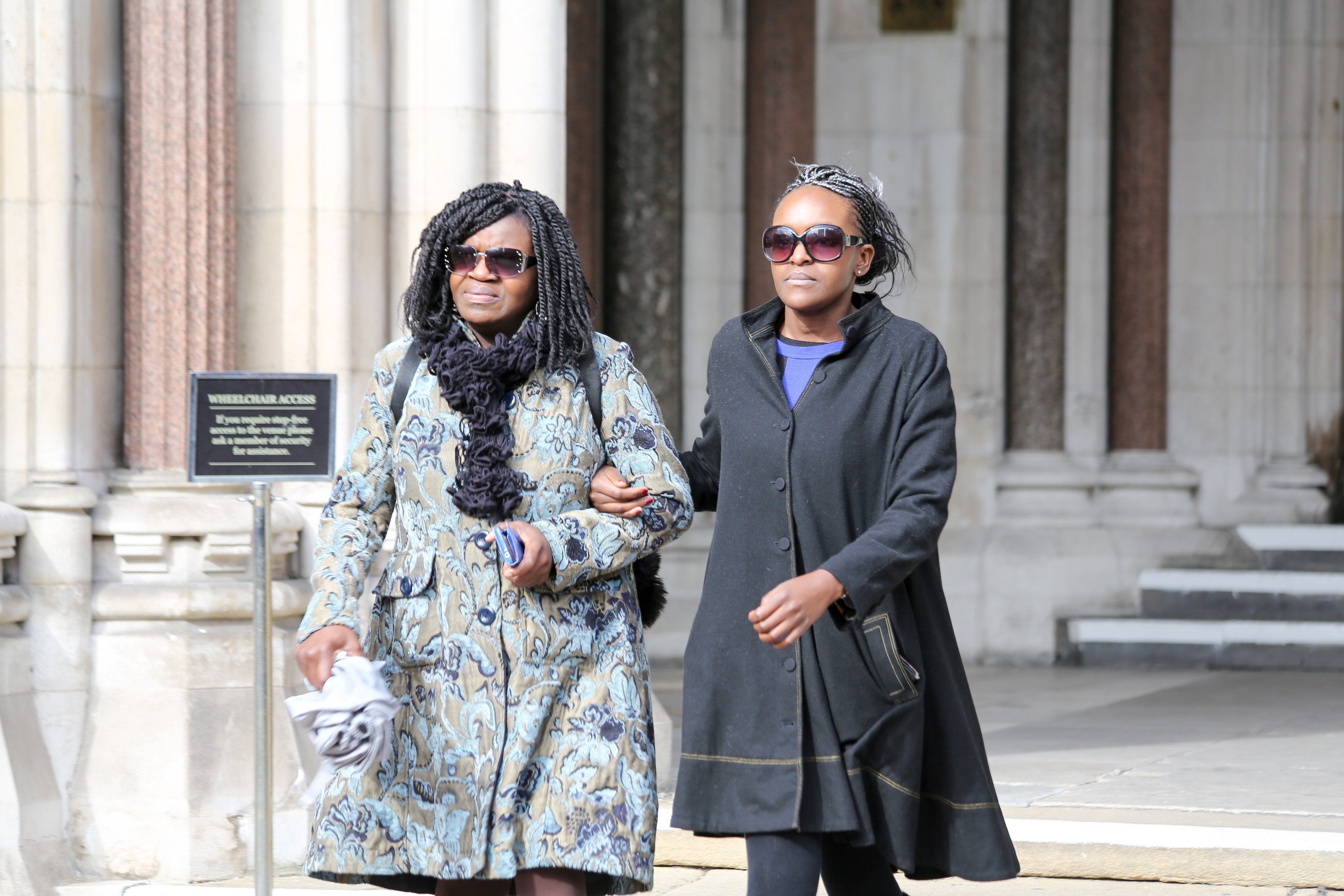 A woman leaves a court precinct, arm in arm with an older woman, both wearing sunglasses