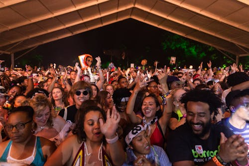 Crowd of diverse people dancing and enjoying a music festival under a large canopy at night, with colourful lights and vibrant atmosphere.
