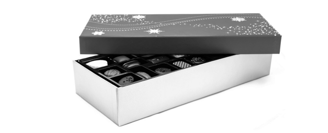 Open box of assorted chocolates with a decorative lid featuring stars and swirls, revealing individually wrapped chocolates inside.