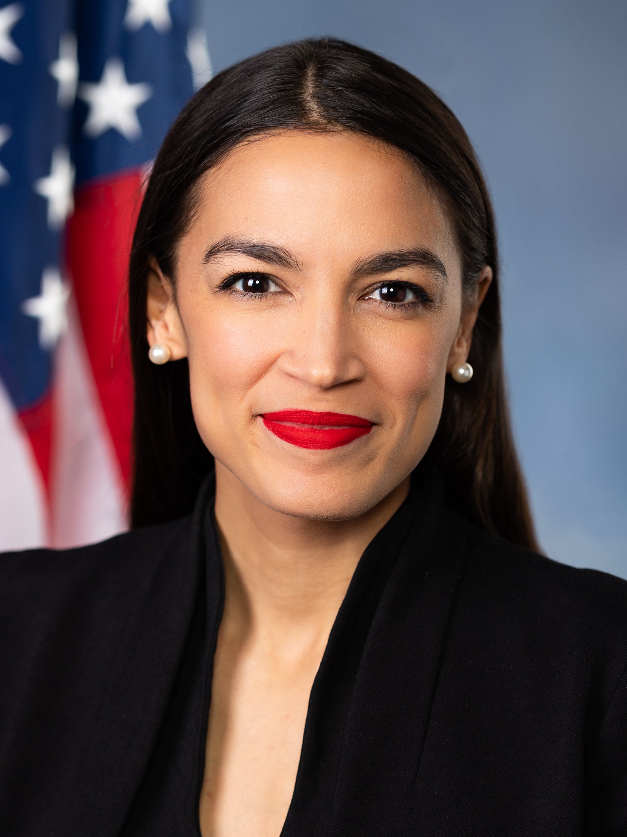 A headshot of a smartly-dressed woman with the US flag in the background