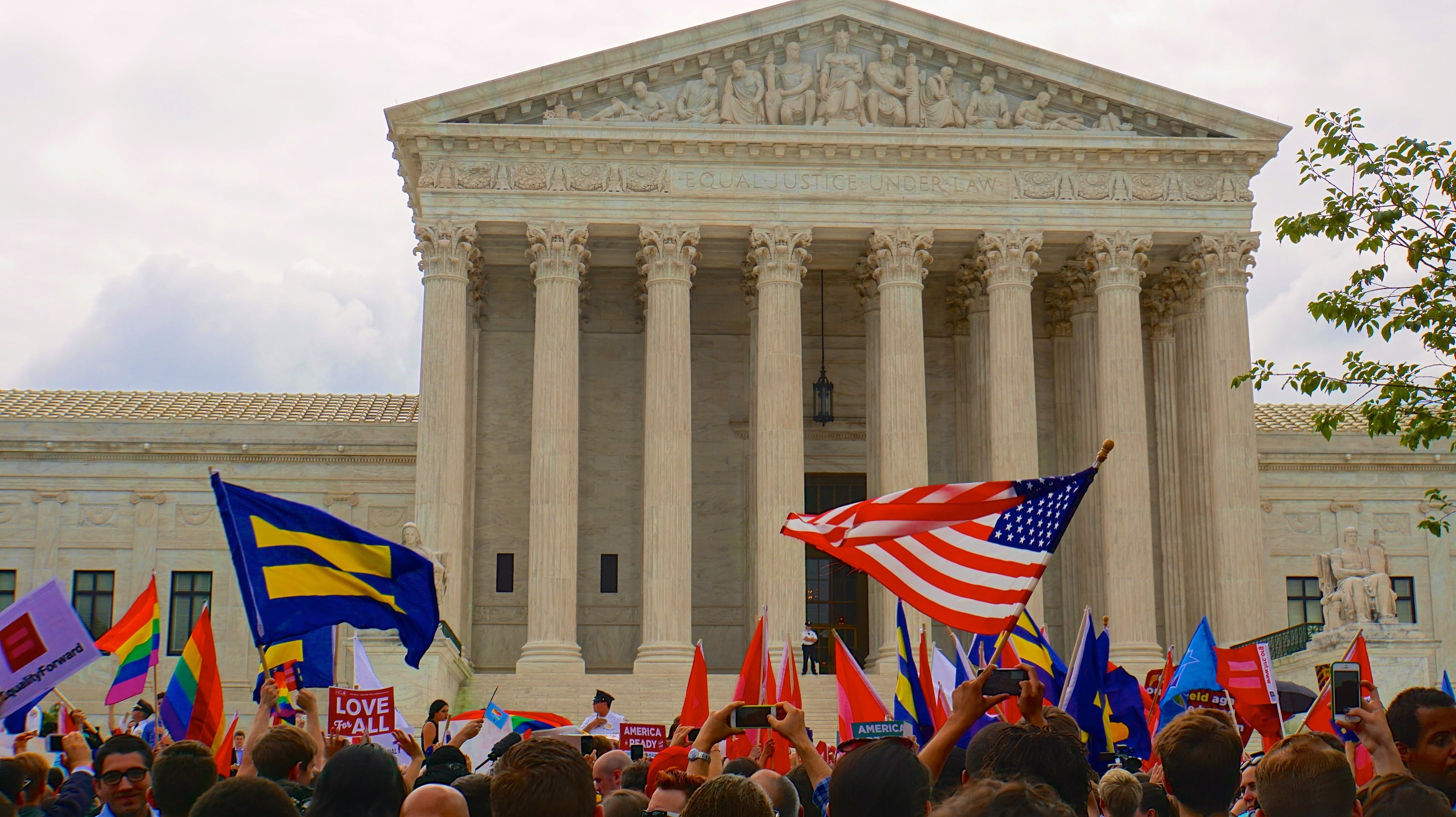 A crowd waving a variety of flags, including the US flag and rainbow flags, outside the US Senate building