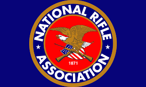 Logo featuring an eagle holding a flag and rifles, centred on a red circle with "National Rifle Association" text, set against a blue background.