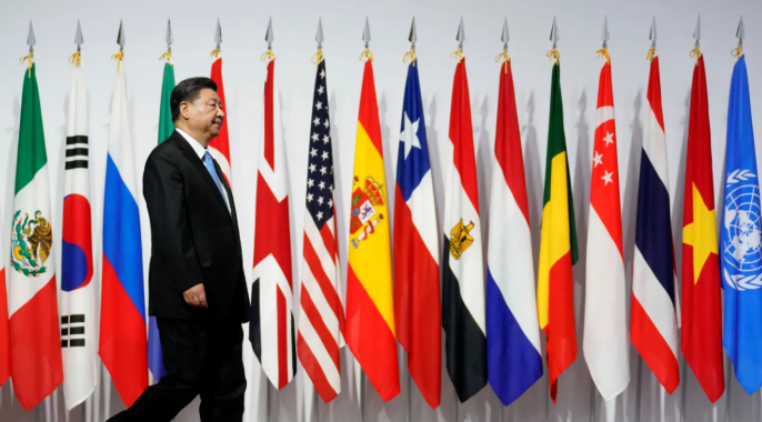 Man in a suit walking past a row of international flags, including those of Mexico, South Korea, and the United Kingdom, on a white background.