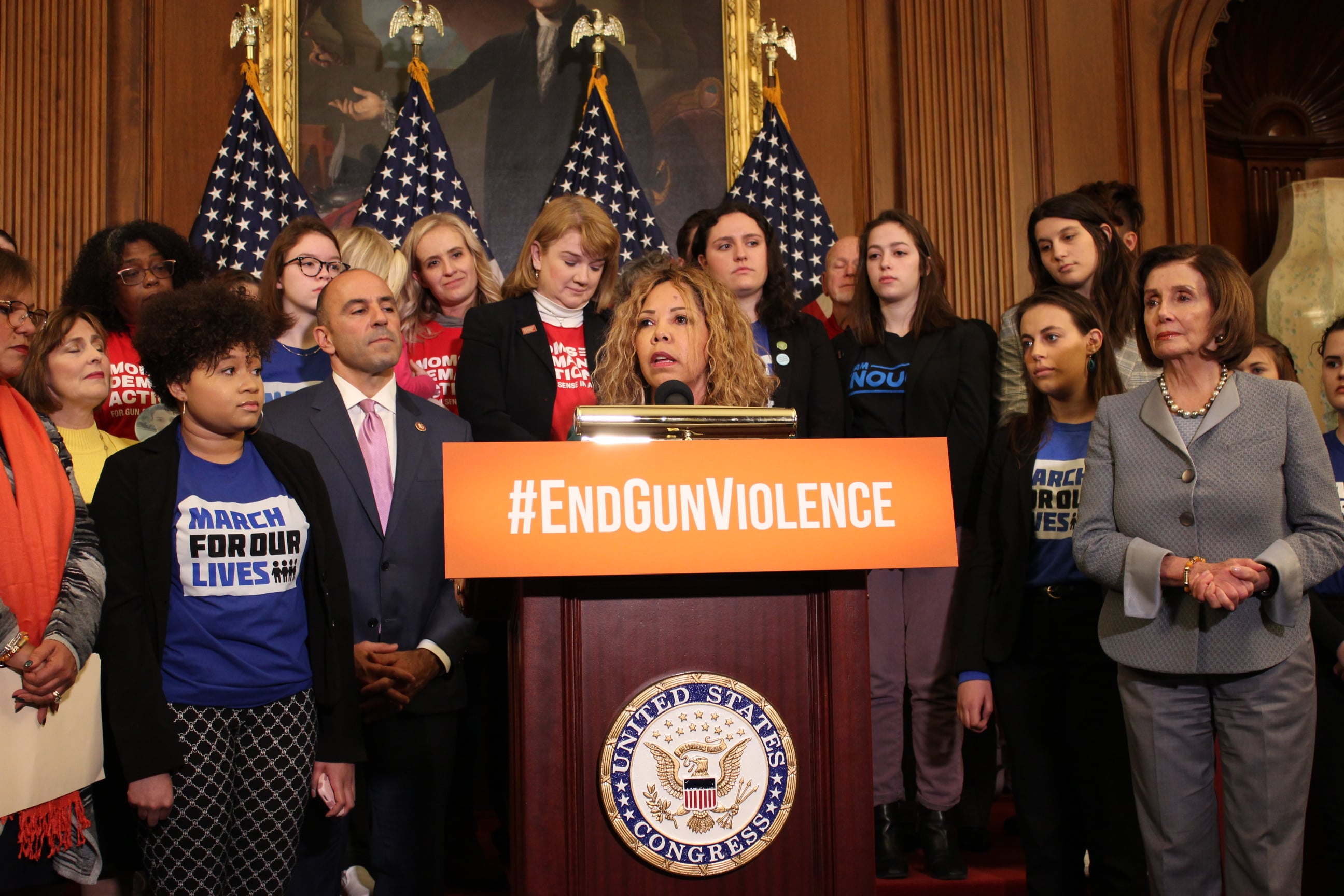 A group of campaigners stand behind a lectern, with the slogan #EndGunViolence