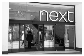Entrance to a Next clothing store with large glass doors and mannequins visible inside. The store name is prominently displayed above the entrance.