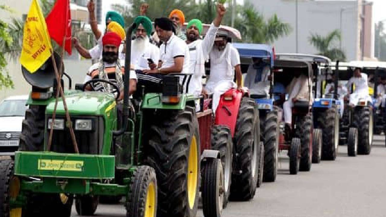 A group of men on tractors participate in a rural protest, holding flags. They are on a street lined with palm trees and buildings.