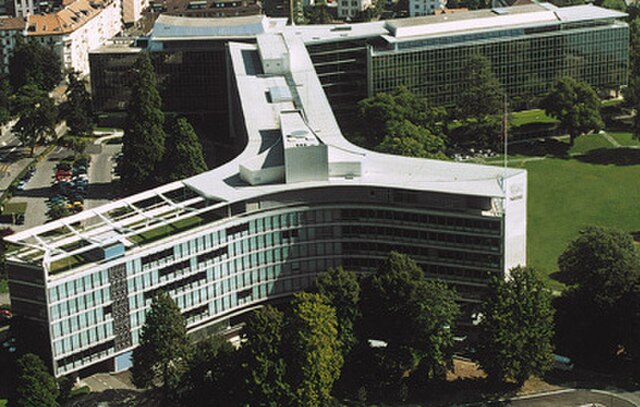 Aerial view of a large, modern office building with a unique Y-shape, surrounded by trees and adjacent structures, under a clear sky.