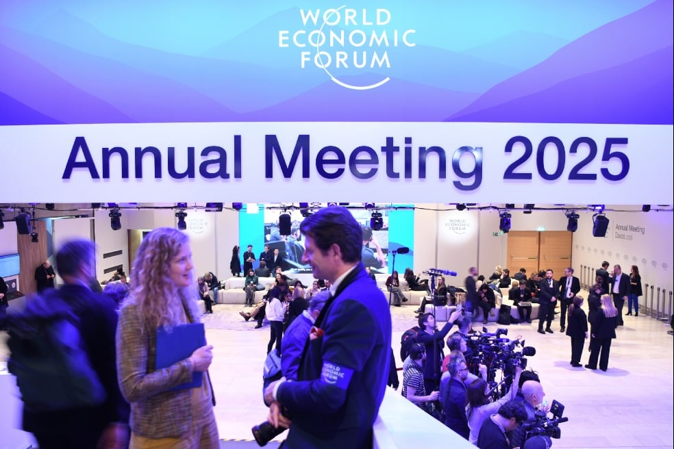 People gather at the World Economic Forum Annual Meeting 2025, featuring large signage and a bustling atmosphere with journalists and attendees.