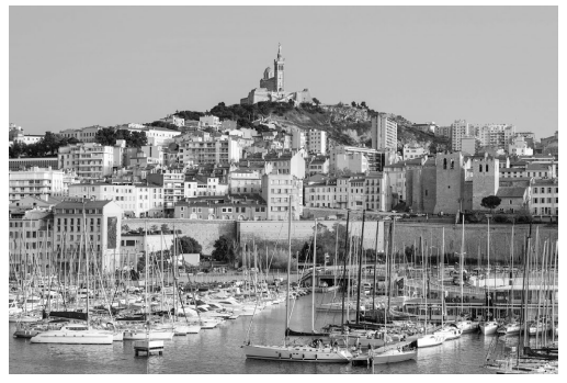 View of a harbour with numerous yachts docked, overlooked by a historic hilltop basilica and surrounded by a cityscape of densely packed buildings.